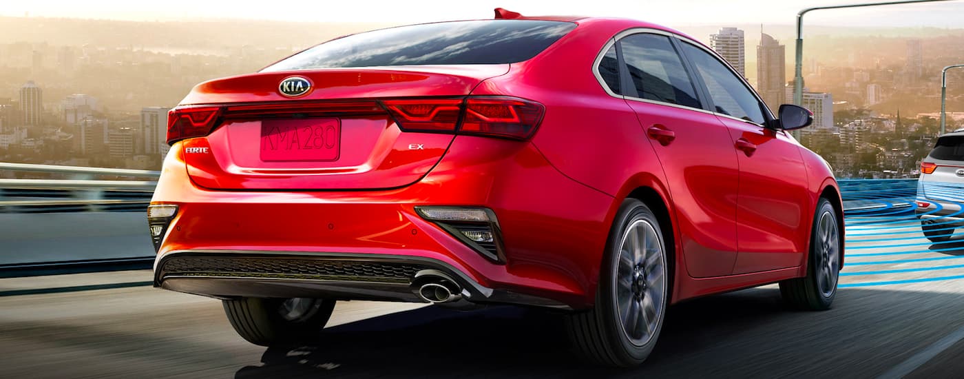 A red 2021 Kia Forte is shown from the rear driving on the highway.