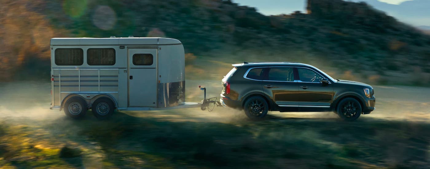 A dark green 2021 Kia Telluride is shown from the side towing an enclosed trailer.