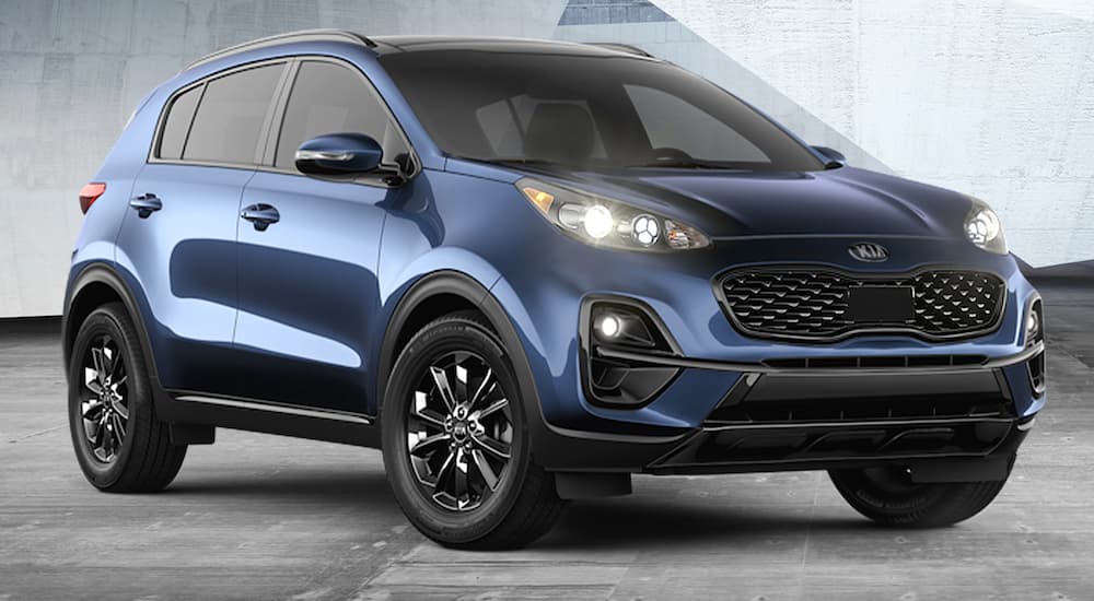A blue 2021 Kia Sportage is parked in front of a concrete wall at a Kia dealer.