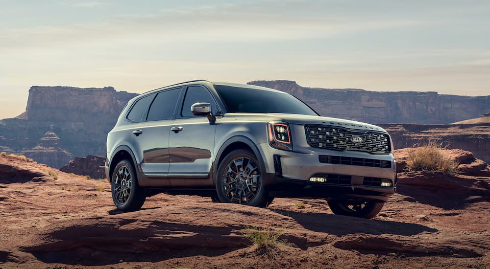 A silver 2021 Kia Telluride is parked off-road in the desert in front of rock formations.