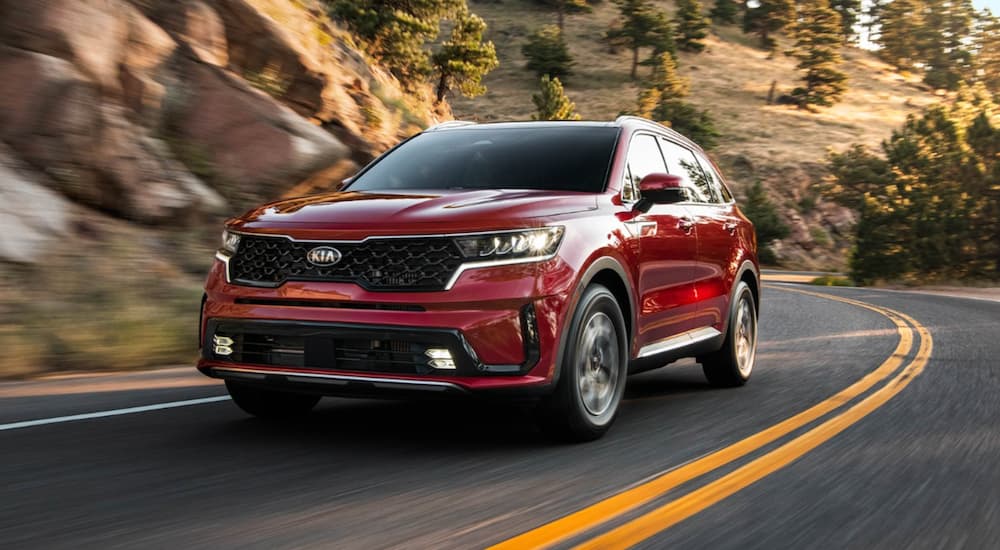 A red 2021 Kia Sorento is driving around a corner past hills.