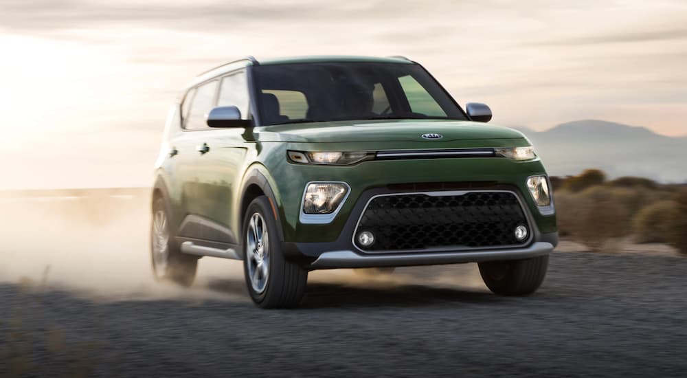 A green 2021 Kia Soul is driving on a desert road kicking up dust.
