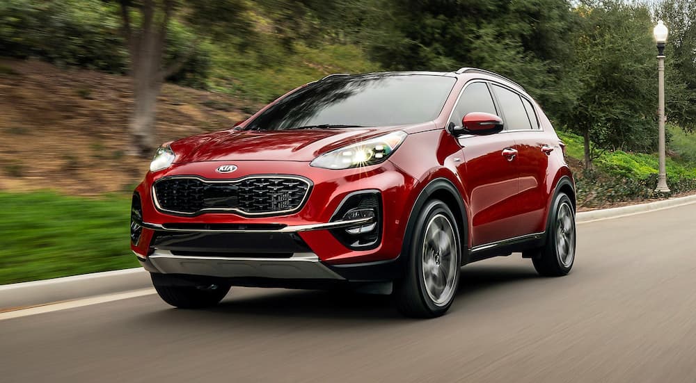 A red 2021 Kia Sportage is driving past shrubs after leaving a Houston Kia Dealer.