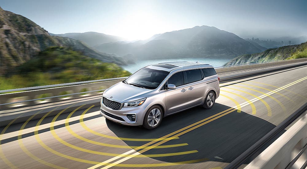 A silver 2021 Kia Sedona with simulated safety lines is driving on a highway.