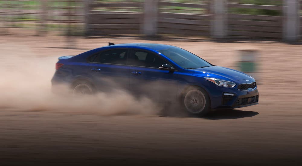 A blue 2021 Kia Forte is driving on a dirt road.