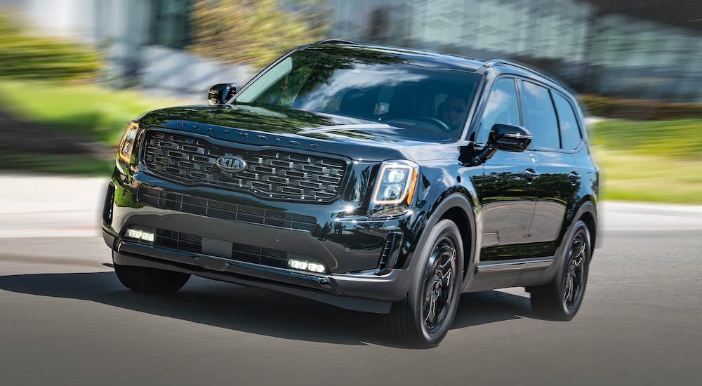 A black 2021 Kia Telluride is driving on a blurred street after leaving a Kia dealer in Houston.