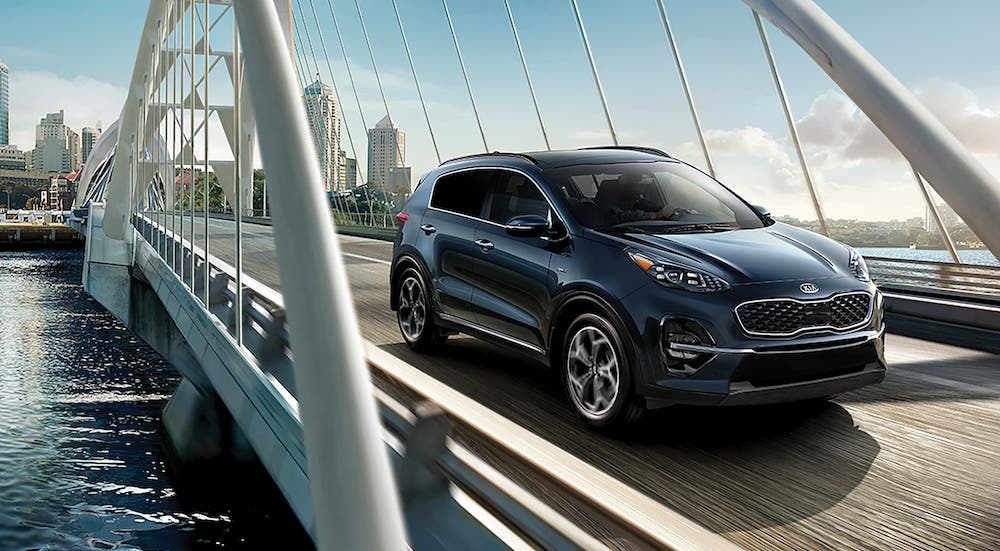 A blue 2021 Kia Sportage is driving over a bridge away from a city.