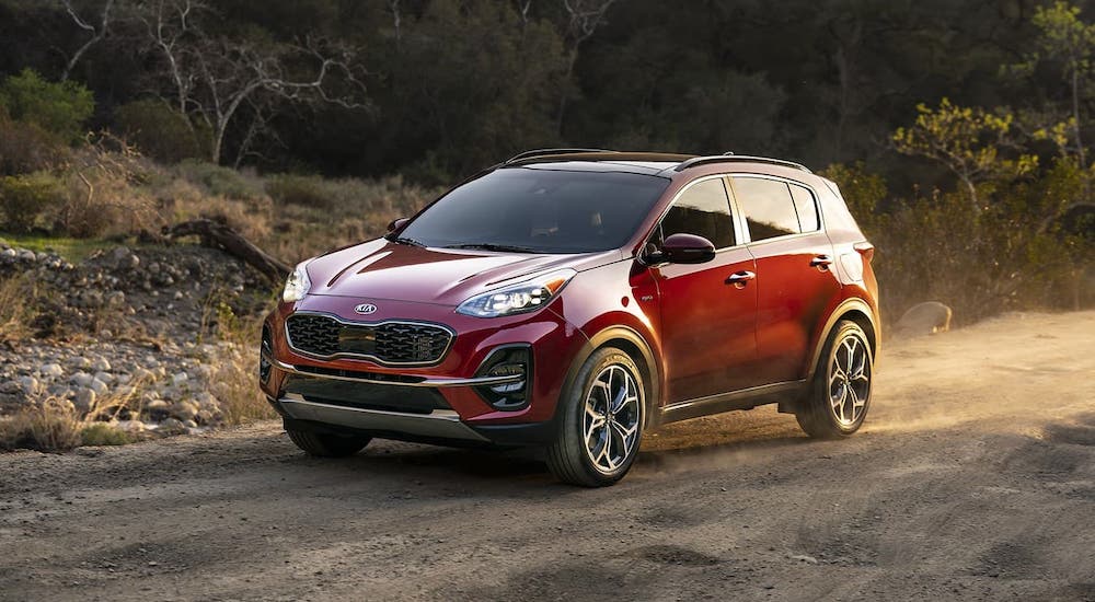 A red 2021 Kia Sportage is driving on a dirt road after leaving a Kia dealership.