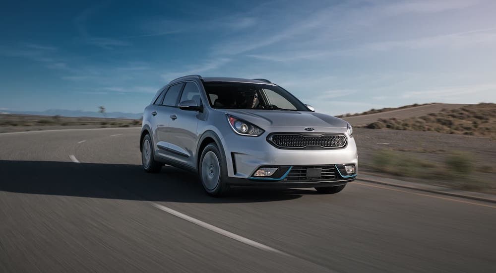 One of the Kia hybrids, a silver 2021 Kia Niro PHEV, is driving on an empty road.