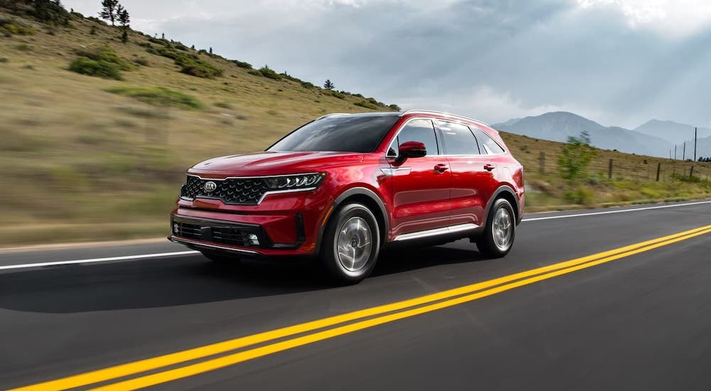 A red 2021 Kia Sorento Hybrid is driving in front of a hill and mountains.