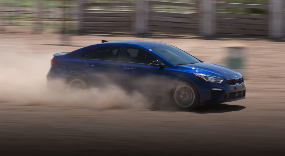 A blue 2021 Kia Forte is shown from the side driving on a dirt track.