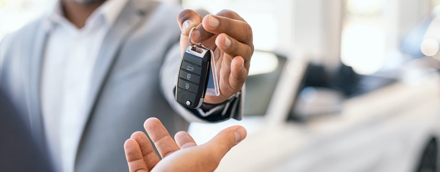A salesman is passing a car key to a buyer at an Atascocita Kia dealer. 