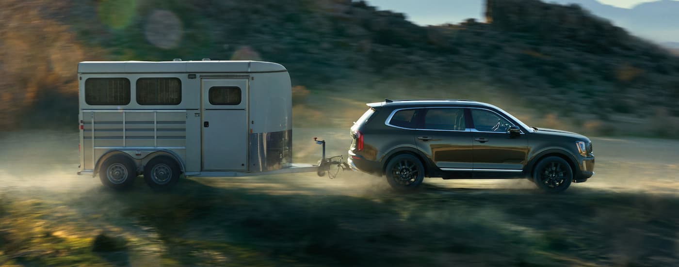 A green 2021 Kia Telluride is towing a horse trailer in front of desert mountains.