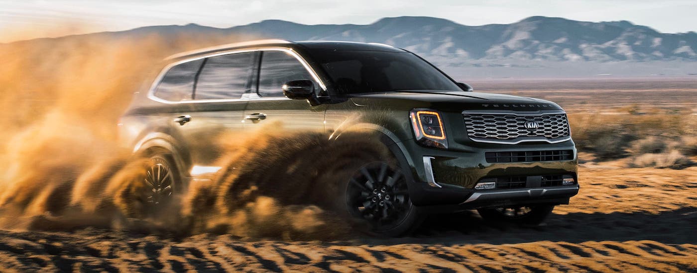 A green 2021 Kia Telluride is kicking up sand in a desert.