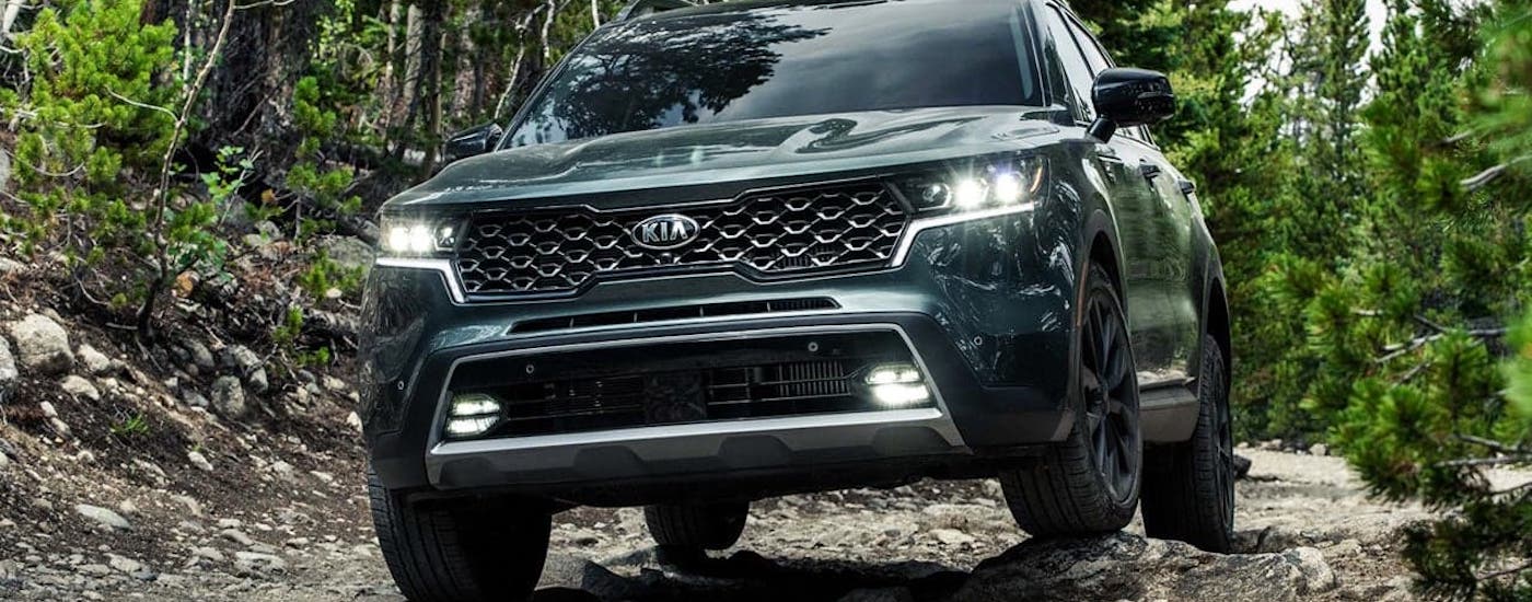 A green 2021 Kia Sorento is in the woods climbing over rocks.