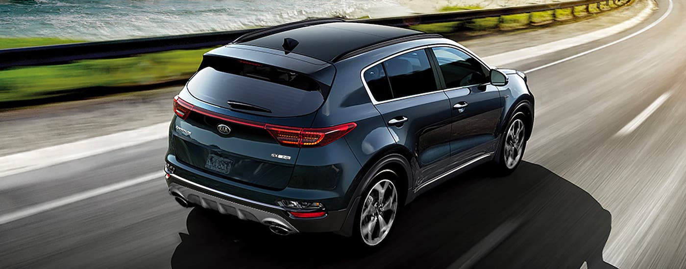 A black 2021 Kia Sportage is driving along a coastal highway and shown from the rear.