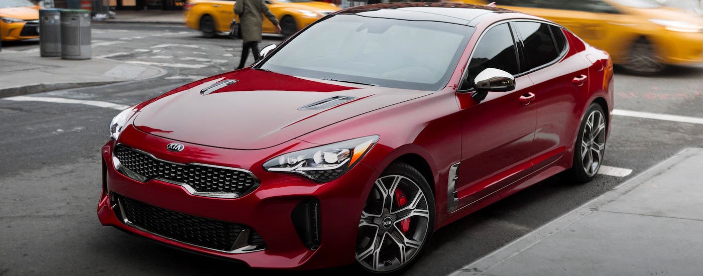 A performance-based Kia model, a red 2021 Kia Stinger, is parked on a city street.