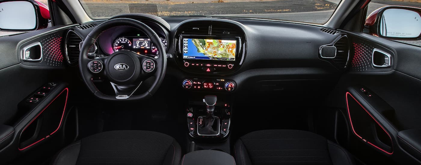The black interior and dashboard of a 2020 Kia Soul is shown with red accents.
