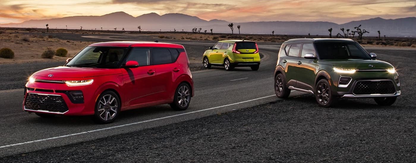 A red, a bright yellow-green, and a dark green 2021 Kia Soul are parked on a race track at sunset.
