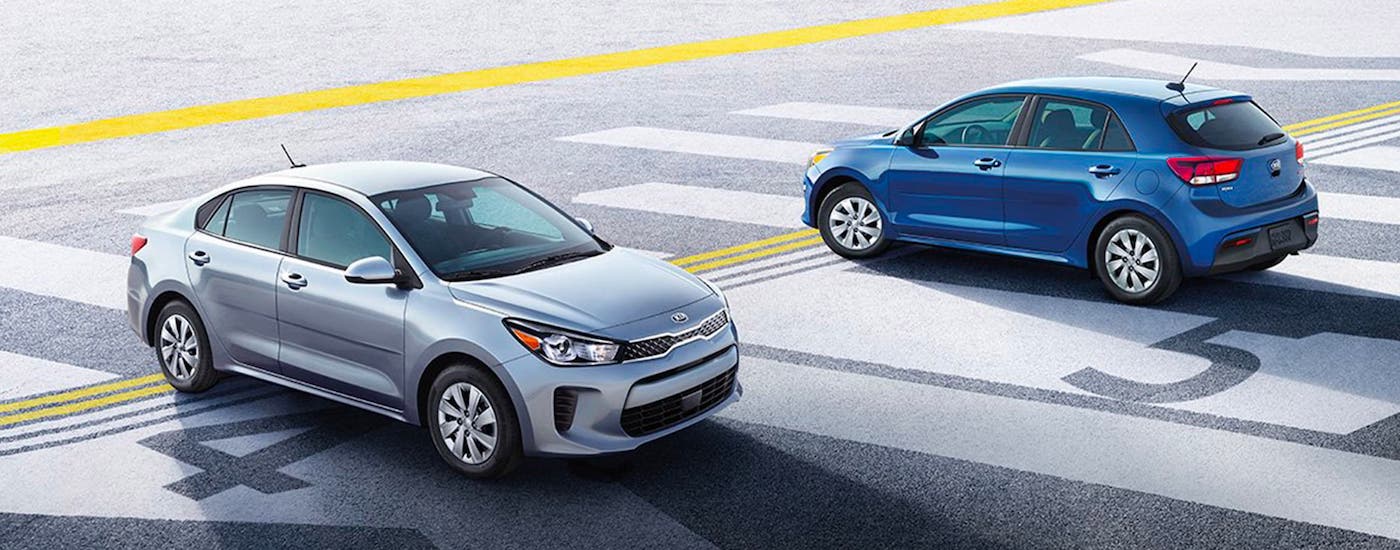 A silver 2020 Kia Forte sedan and a blue hatchback are parked on a runway.